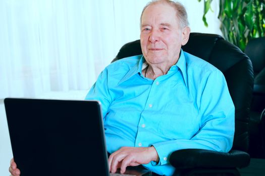 Elderly man using laptop computer sitting in leather recliner