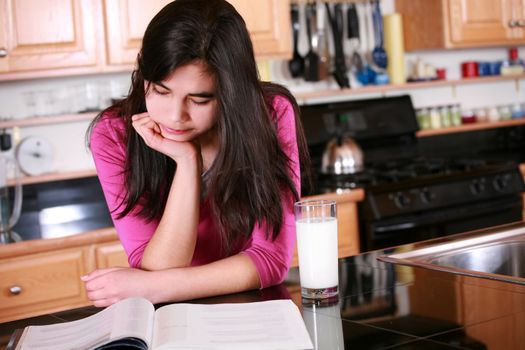 Teen girl relaxing in kitchen with magazine and glass of milk