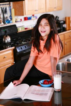 Young girl sitting on kitchen counter with glass of milk