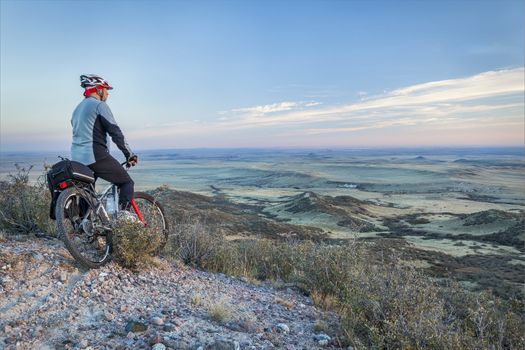 senior male on a mountain bike contemplating a view of rolling prairie at dusk, Soapstone Prairie Natural Area near Fort Collins, Colorado