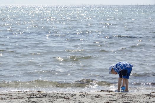 Boy playing with sand and water at the beach of Denmark