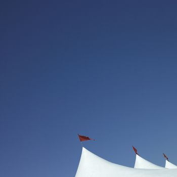 White tent swith red flags against blue sky
