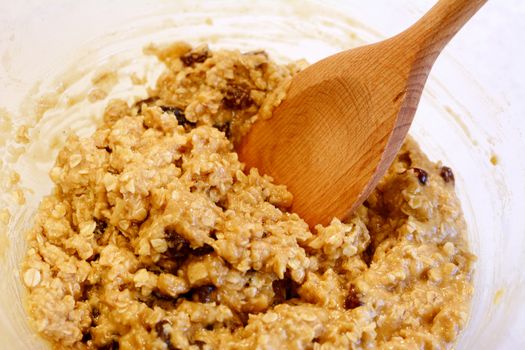Closeup of oatmeal raisin cookie dough being mixed with a wooden spoon