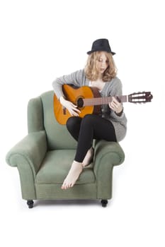 young pretty woman playing guitar on side of armchair against white background