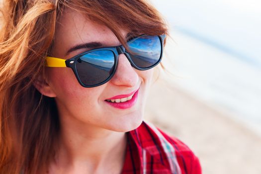 Portrait of a pretty fashionable, young woman in a chequered red shirt and sunglasses on the beach