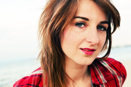 Portrait of a pretty fashionable, young woman in a chequered red shirt on the beach