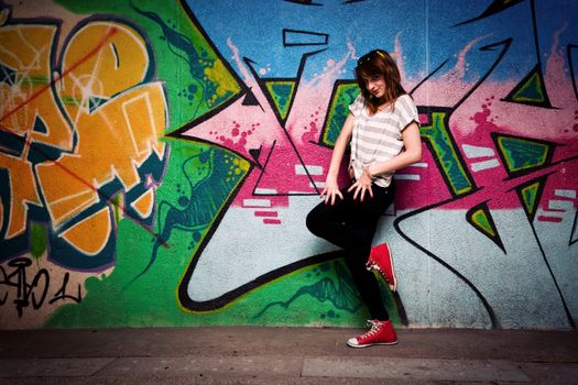 Stylish fashionable girl in a dance pose against colorful graffiti wall. Fashion, trends, subculture. Full body shot