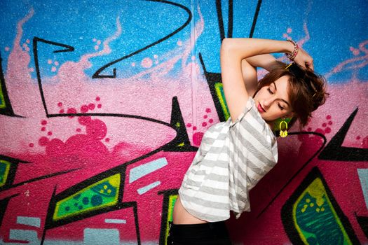 Stylish fashionable girl in a dance pose against colorful graffiti wall. Fashion, trends, subculture.