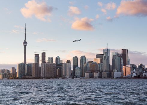 Toronto skyline at sunset with a small turbo prop aircraft plane flying over city as it comes in to land at Billy Bishop airport near downtown