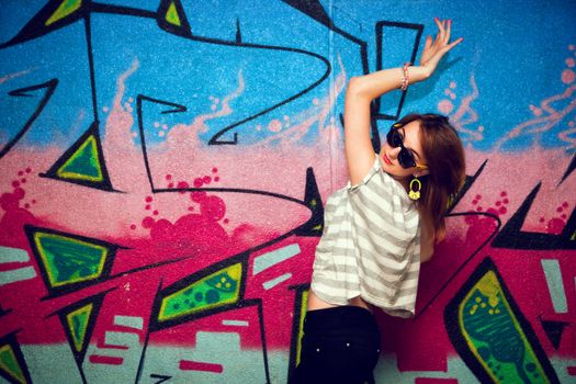Stylish fashionable girl in a dance pose against colorful graffiti wall. Fashion, trends, subculture.
