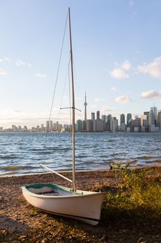 Single sailing boat beached on sandy shore of Lake Ontario on Wade Island of Toronto Islands with skyline of city in the background