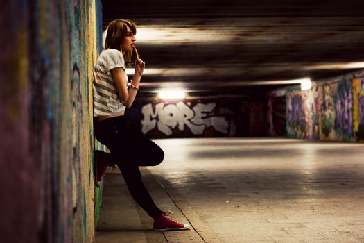 Stylish young girl standing in grunge graffiti tunnel, shanty town. Fashion, trends, subculture. Full body shot