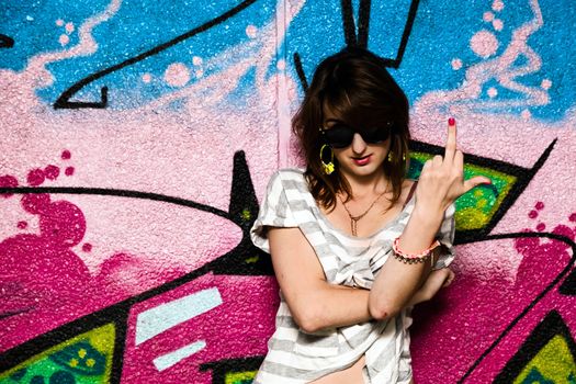 Stylish fashionable girl showing fuck off middle finger gesture against colorful graffiti wall.