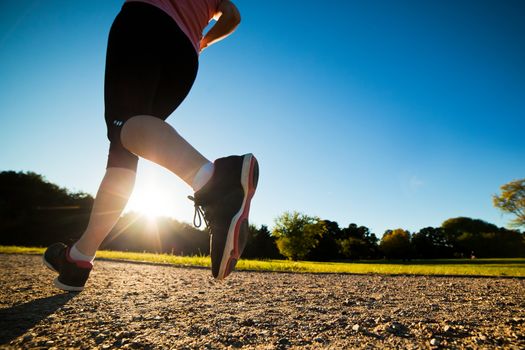 Young fit woman does running, jogging training in a park at summer sunny day. Legs close up