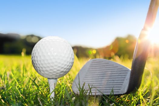 Golf ball on white tee and golf club preparing to shot. Green grass golf course. Blue sunny sky