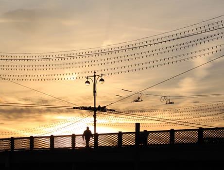 A man walks across the bridge at sunset