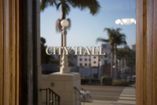 A door leading inside of a southern California City Hall building. Palm trees and the street are visible in the reflection of the glass door.