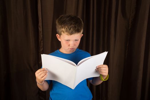 A young boy reading a book that is blank to apply your own design on. This young boy is about 9 years old.