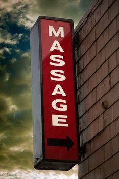 Sign attached to a shingle sided building pointing to a massage parlor.