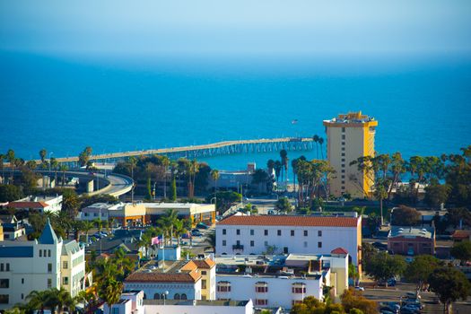 A beautiful view of the Pacific Ocean and the City of Ventura, California. A view of the pier, a high rise hotel, and Spanish style architecture fill the scene.