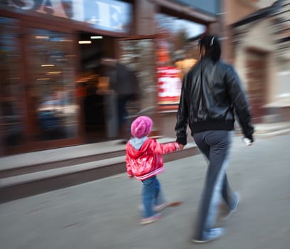 A young mother and her daughter walk past a store with a sellout. Intentional motion blur