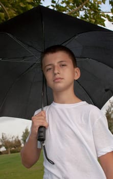 Boy looking at camera while under umbrella outside  .