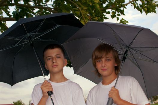 Portrait of happy boys looking at camera while under umbrella outside .
