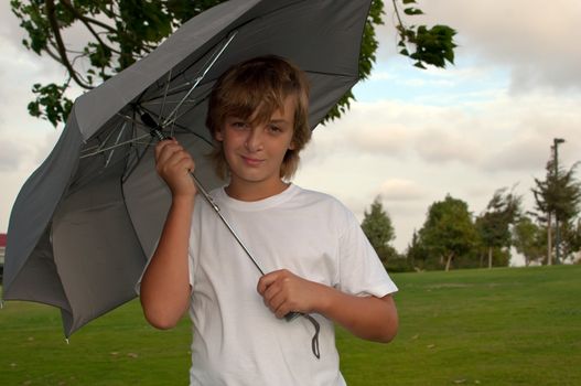 Boy looking at camera while under umbrella outside  .