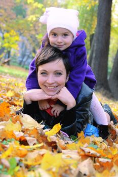 Happy mother and little daughter lying among autumn leaves