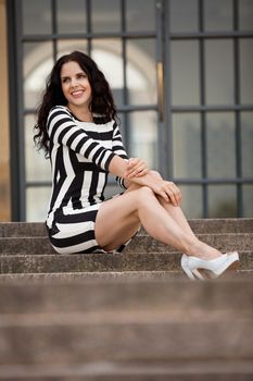 attractive woman in sexy dress in stripes sitting on stairs