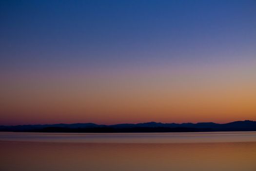 This beautiful sunset over water is photographed in an abstract way to show the color and lines of the land across the lake.