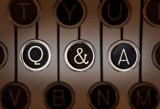 Close up of old manual typewriter keyboard with scratched chrome keys that spell out "Q & A". Lighting and focus are centered on "Q & A" keys. 