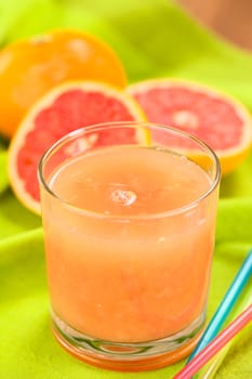 Freshly squeezed juice of the pink-fleshed grapefruit with colorful drinking straws on the side and grapefruits in the back on green fabric (Selective Focus, Focus on the bubble on the middle of the juice)