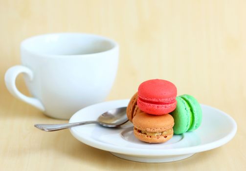 Colorful macaroons and a cup of coffee with spoon