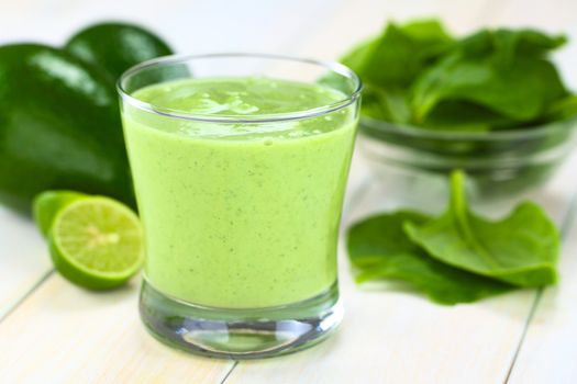 Healthy refreshing green smoothie made of fresh avocado, spinach, lime and yoghurt in a glass on bright wood (Selective Focus, Focus on the front of the glass rim)