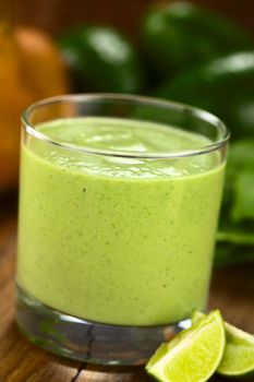 Healthy refreshing green smoothie made of fresh avocado, spinach, lime, pear and yoghurt in a glass on dark wood (Selective Focus, Focus on the front of the glass rim)