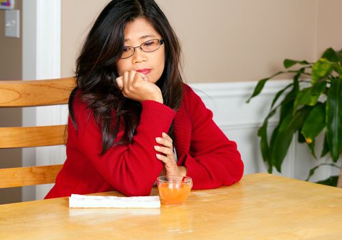 Asian woman relaxing at dining table with glass of juice, sad or lonely expression
