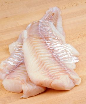 Two Slices of Raw Fresh Cod Fish Fillet closeup on Wooden Cutting Board