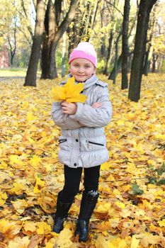 little girl with yellow leaves standing in the park