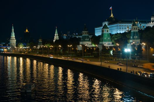 A night view of the Moscow city Kremlin with an illuminated river and a boat.