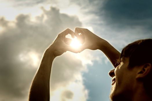 Toned Photo of Teenager with Hands in Heart Shape on Sky Background