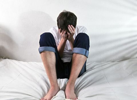 Sad Young Man sitting on the bed in home interior