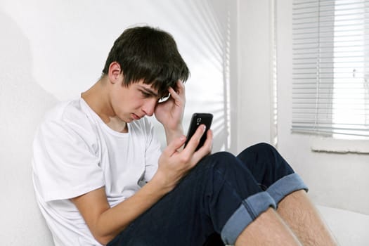 Sad Young Man with Cellphone sitting on the bed