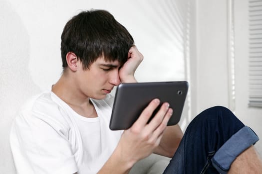 Sad and Tired Young Man with Tablet Computer sitting on the bed