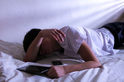 Tired Young Man Sleeps with Tablet Computer on the bed In the Dark Room