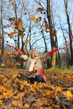 Happy blond girl with autumn leaves in park