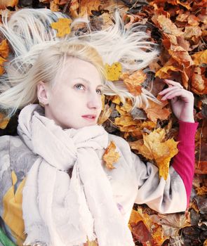 Pretty girl with blond hair lying on autumn leaves