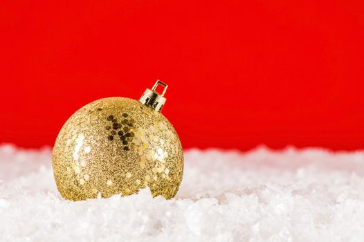 Golden Christmas decoration in artificial snow on red backgtound