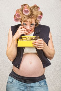 Smiling pregnant lady in curlers eating chocolates