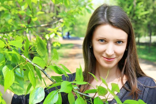 Young beautiful smiling through the branches of green tree